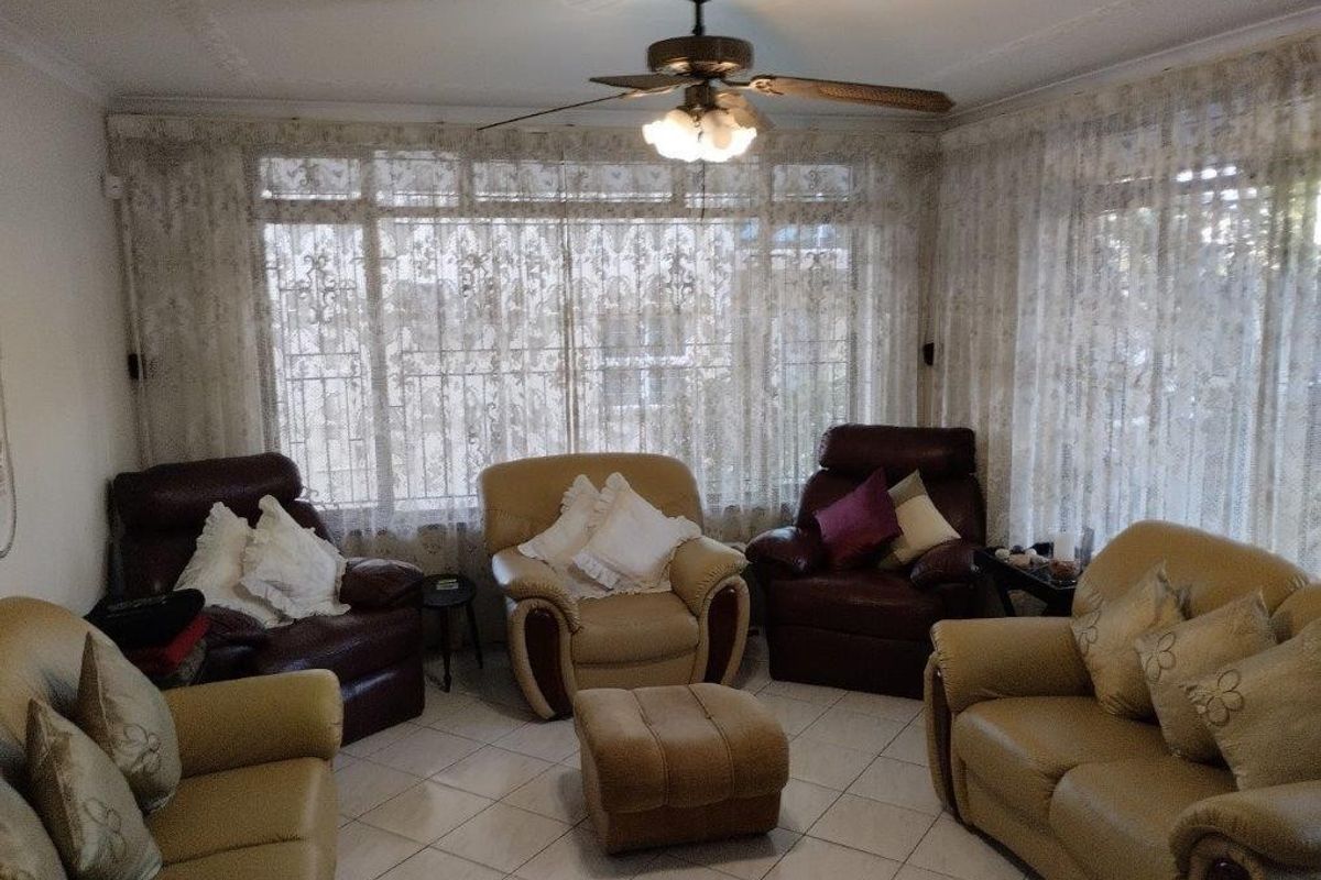 A living room featuring tiled flooring, a ceiling fan, and large windows with decorative curtains, providing a functional and well-lit space.