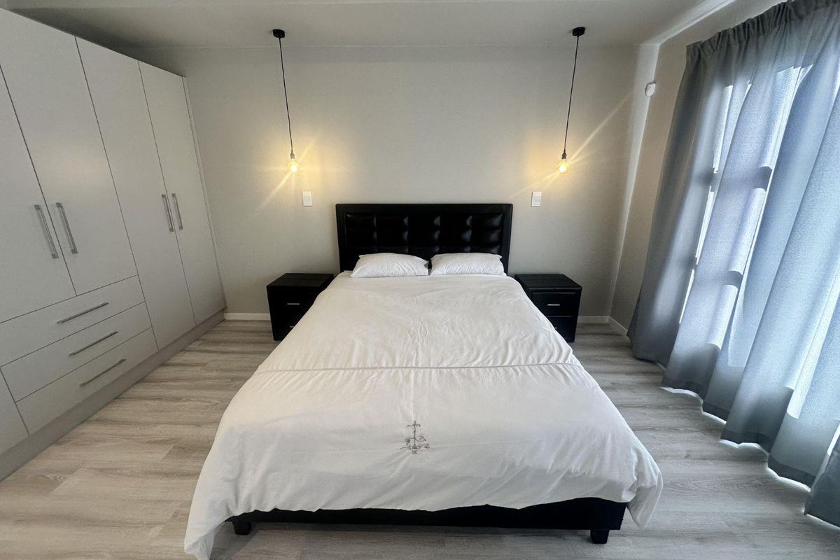 A well-maintained bedroom featuring built-in wardrobes, modern pendant lighting, and light-toned laminate flooring.
