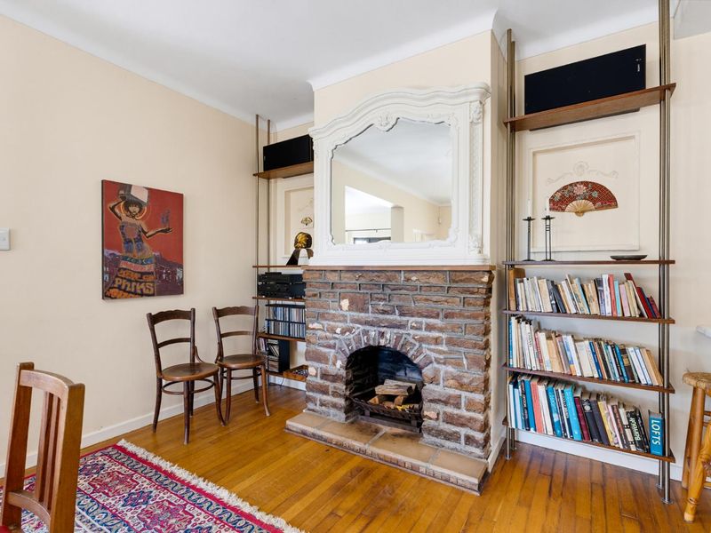 A living room featuring a traditional brick fireplace, hardwood flooring, and built-in shelving units, creating a cozy and character-filled space.