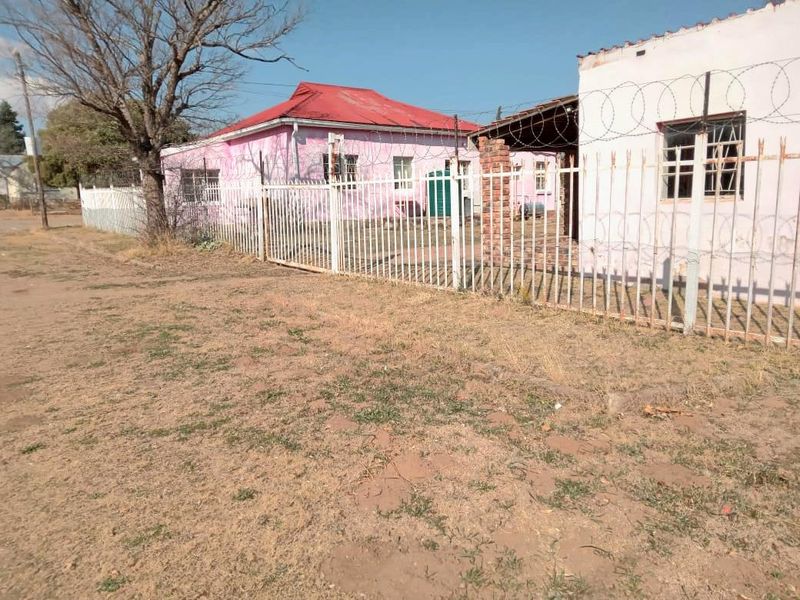Front exterior view of a residential property featuring metal security fencing with razor wire and a covered patio area.