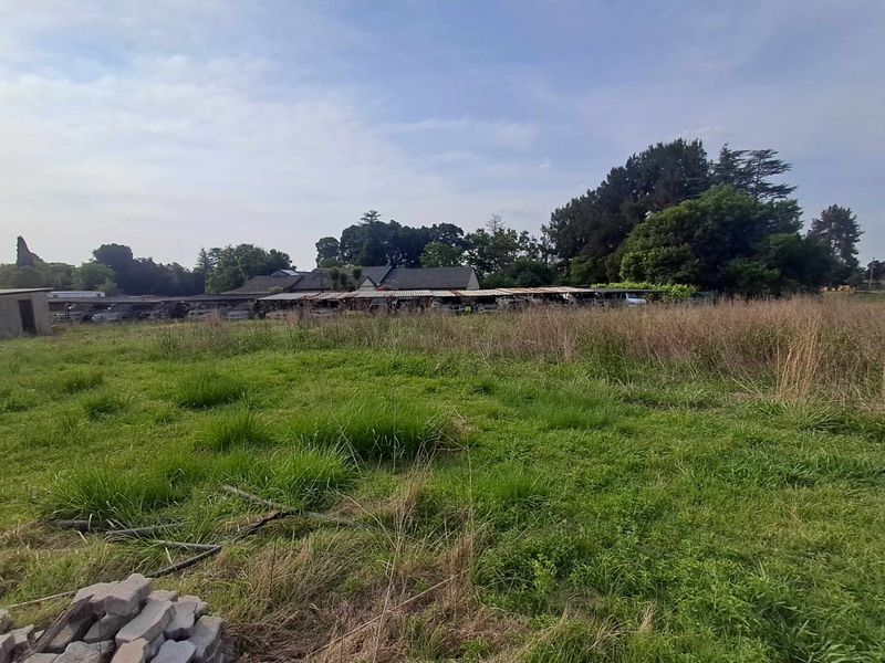A wide view of the property grounds featuring open land, overgrown grass, and a series of outbuildings with corrugated metal roofing.