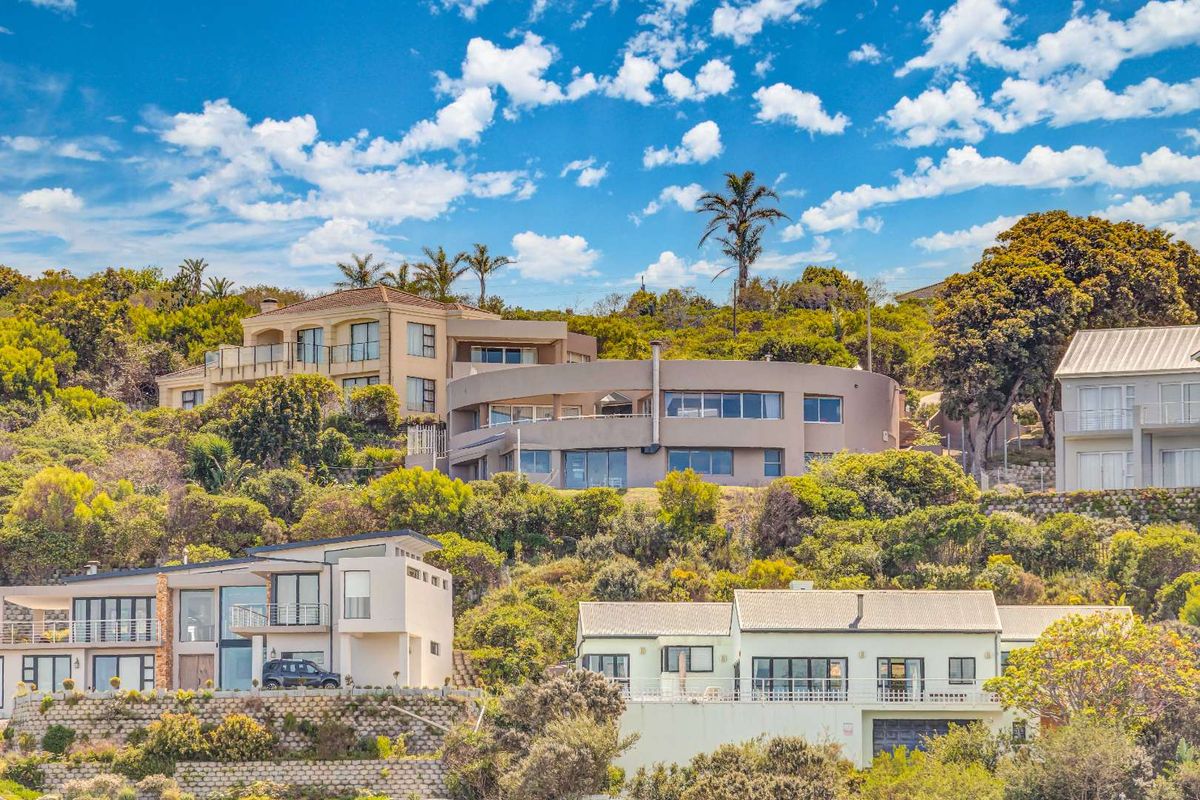 An elevated view of a multi-level residential property nestled into a hillside, showcasing modern architectural design and extensive surrounding greenery.
