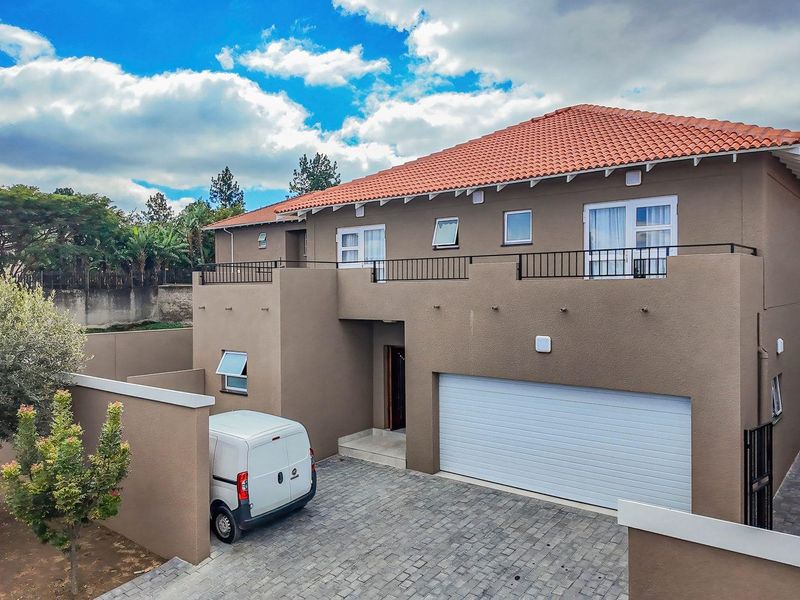 Front elevation of a double-story cluster home featuring a tiled roof, paved driveway, double garage, and an upper-level balcony with metal railings.