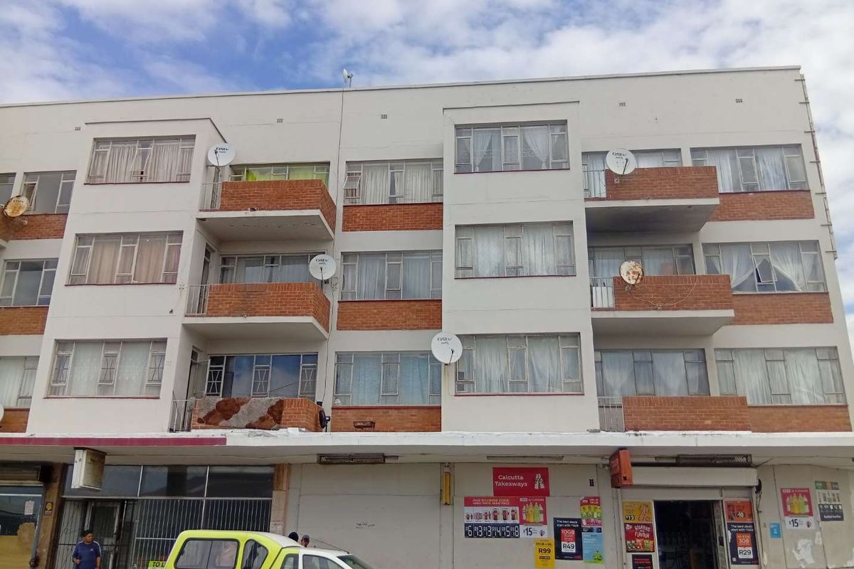 Front elevation of a multi-story apartment building featuring brick balconies, aluminium windows, and ground-floor commercial retail space.