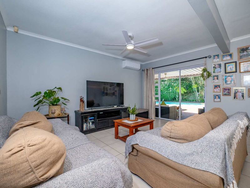 A bright living room featuring tiled flooring, a ceiling fan, and a split-system air conditioner, with direct access to the outdoor patio area.