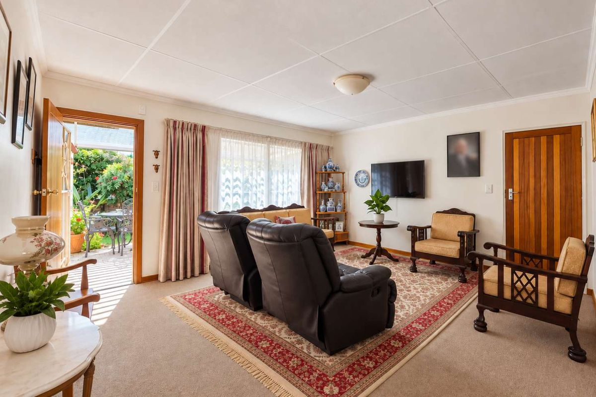 A comfortable living room featuring carpeted flooring, a tiled ceiling, and direct access to an outdoor patio area through a sliding glass door.