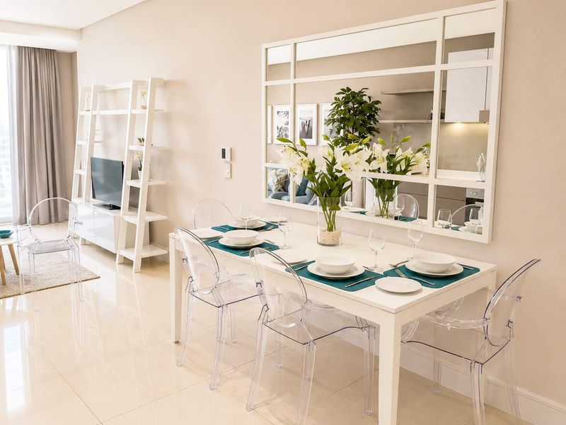 A bright and modern open-plan living and dining area featuring polished tiled flooring, neutral walls, and a large decorative wall mirror.
