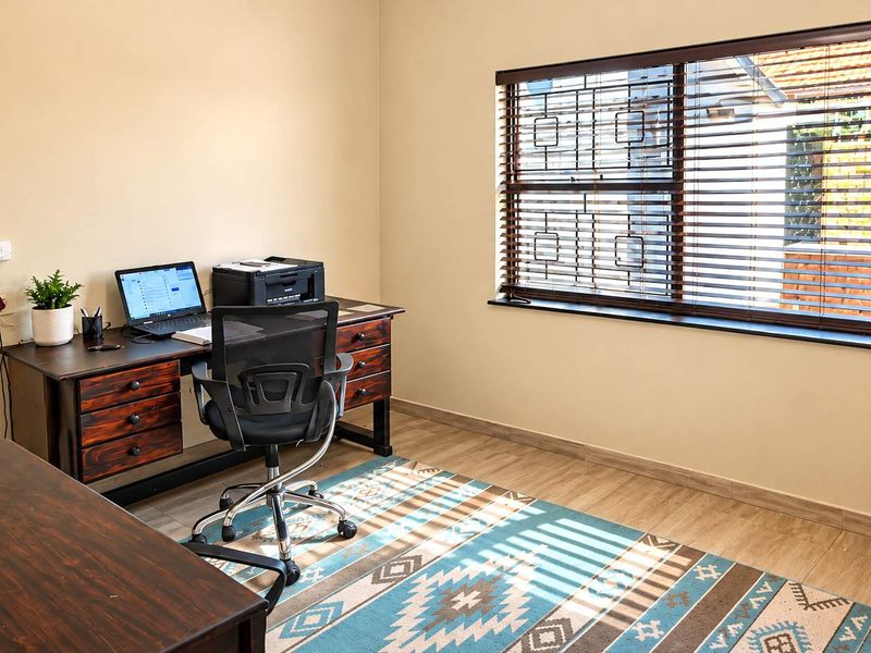 A functional home office featuring laminate flooring, venetian blinds, and security bars on the window, providing a bright and practical workspace.