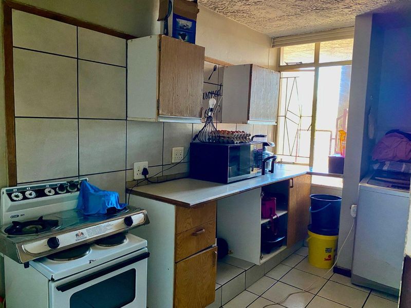 A functional kitchen featuring tiled flooring, a tiled backsplash, built-in cabinetry, and a freestanding stove, with a window providing natural light.