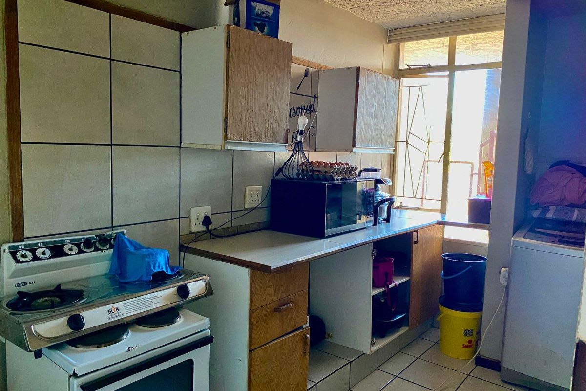 A functional kitchen featuring tiled flooring, a tiled backsplash, built-in cabinetry, and a freestanding stove, with a window providing natural light.
