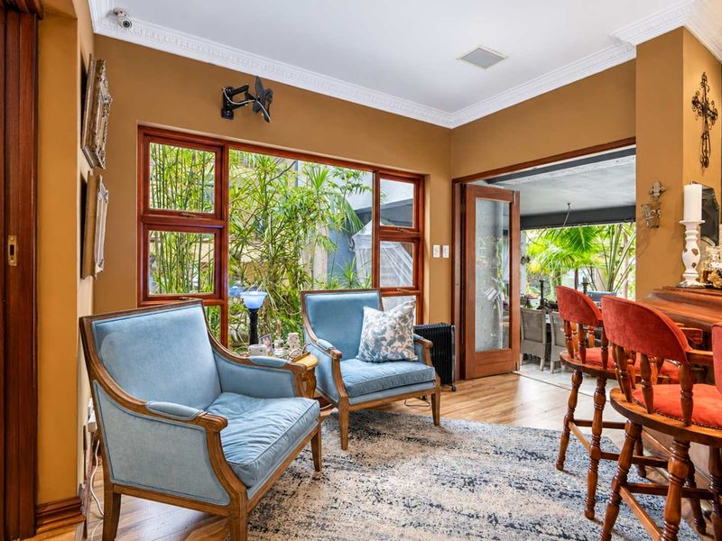A cozy living area featuring hardwood flooring, crown molding, and large wooden-framed windows that provide a view of the outdoor patio area.