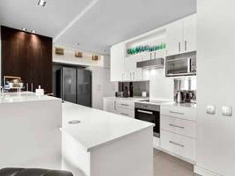 Modern kitchen featuring sleek white cabinetry, stone countertops, integrated appliances, and a functional island, illuminated by recessed lighting.