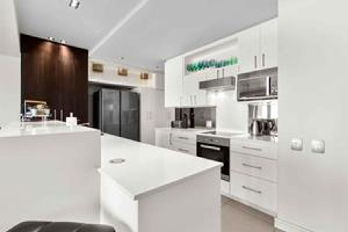Modern kitchen featuring sleek white cabinetry, stone countertops, integrated appliances, and a functional island, illuminated by recessed lighting.