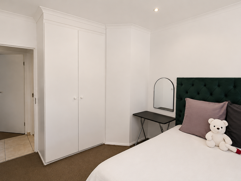 A well-maintained bedroom featuring neutral walls, carpeted flooring, recessed lighting, and a built-in wardrobe, with an adjacent hallway visible through the open door.