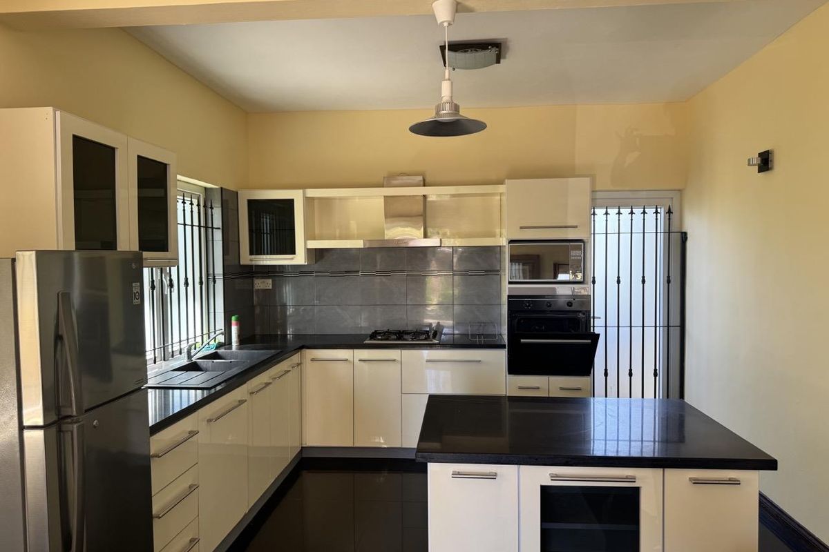 Modern kitchen featuring high-gloss cabinetry, dark stone countertops, a central island, built-in oven, and stainless steel extractor fan.