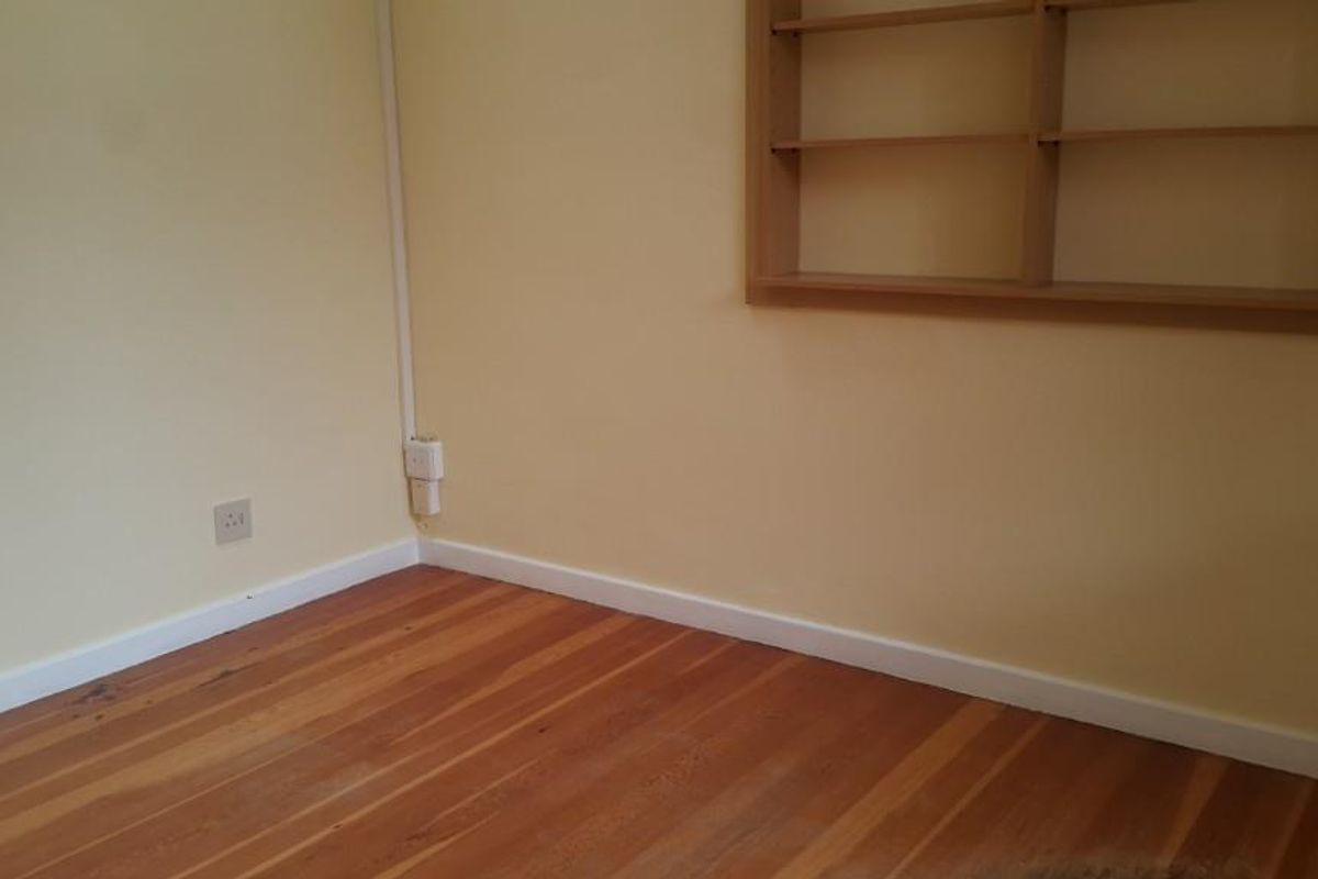 A bright bedroom featuring polished timber flooring, built-in wall shelving, and neutral wall finishes.
