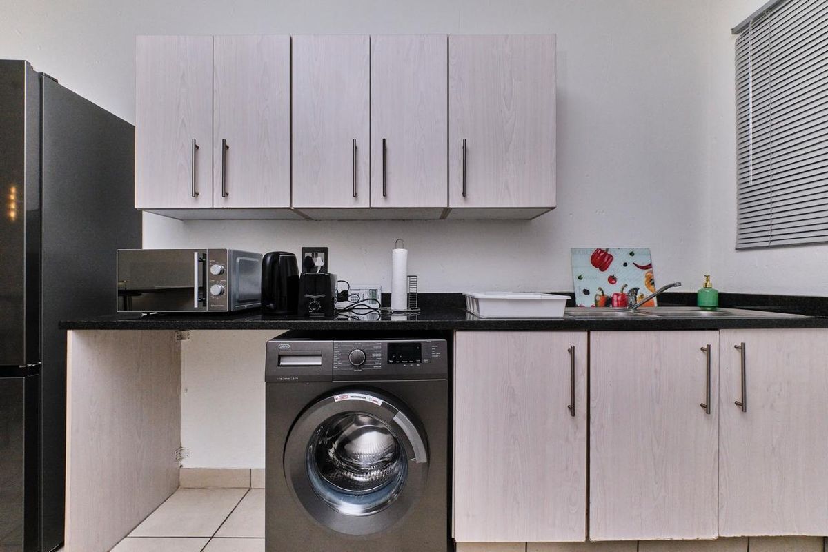 A functional kitchen area featuring light wood-finish cabinetry, dark granite countertops, a stainless steel sink, and space for a washing machine.