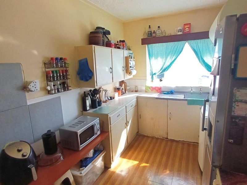 A compact kitchen featuring dated cabinetry, laminate countertops, and a stainless steel sink, offering potential for a modern renovation.