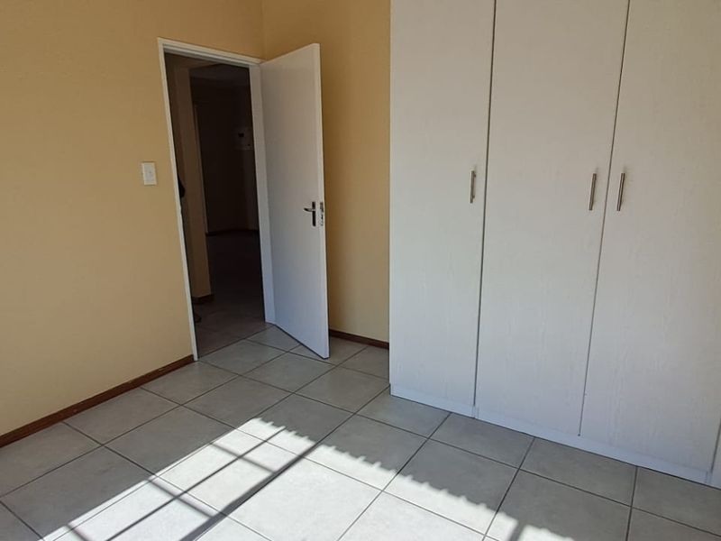 A clean, empty bedroom featuring neutral tiled flooring and built-in white cupboards, offering a blank canvas for personalization.
