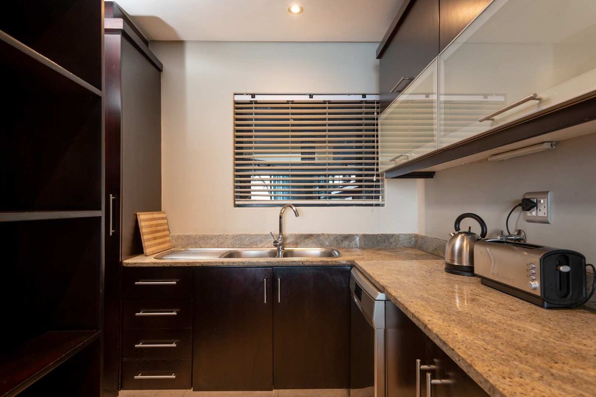 A well-maintained kitchen featuring dark wood cabinetry, granite countertops, a stainless steel sink, and integrated dishwasher, complemented by modern recessed lighting.