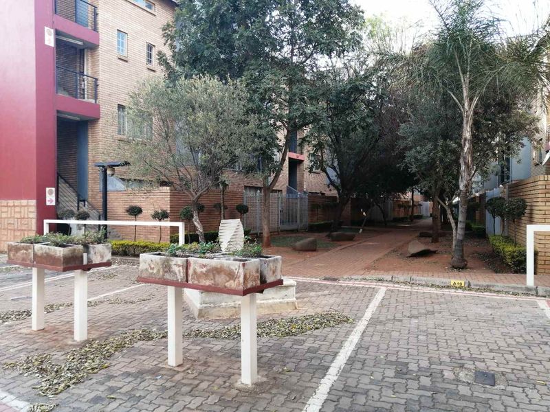 Exterior view of an apartment complex featuring a brick facade, paved driveway, and established garden area with concrete planters.