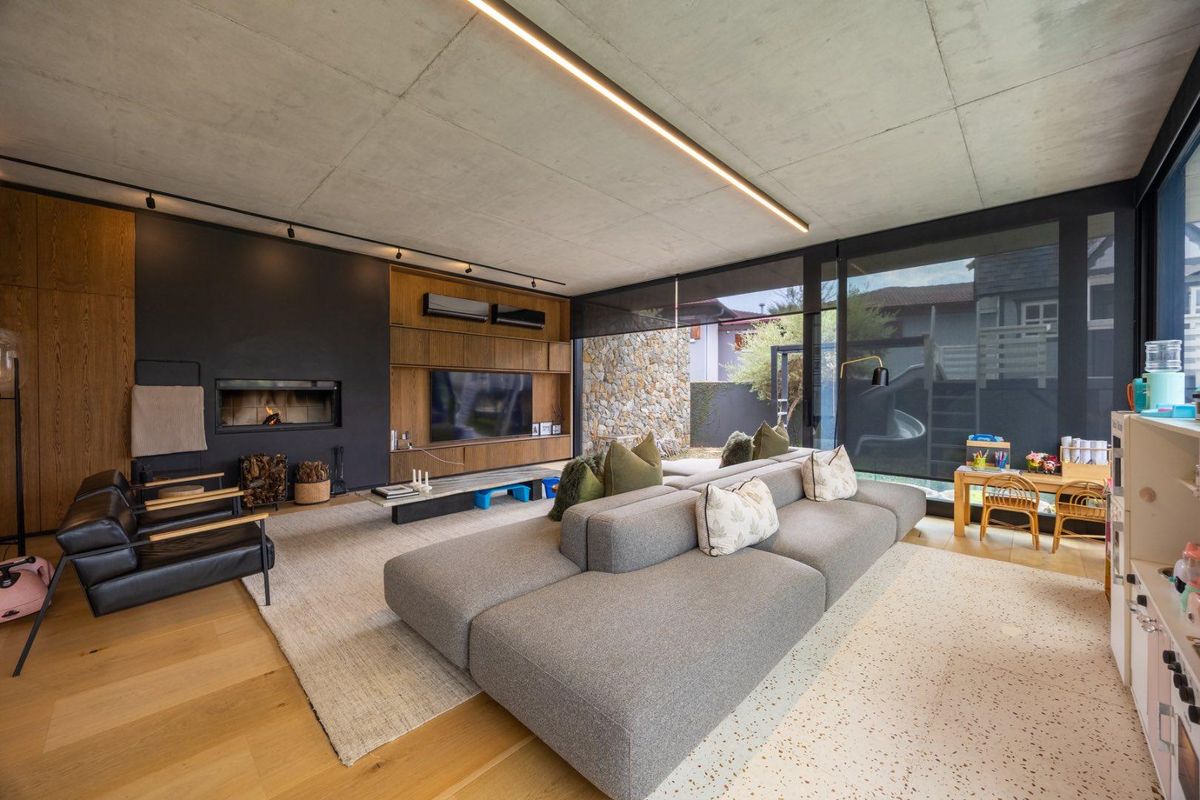 Modern living room featuring an exposed concrete ceiling, built-in fireplace, timber wall paneling, and large sliding glass doors opening to an outdoor area.