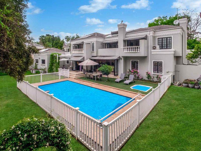 Spacious rear exterior view featuring a well-maintained swimming pool with safety fencing, a paved patio area, and a large two-story residence with balconies.