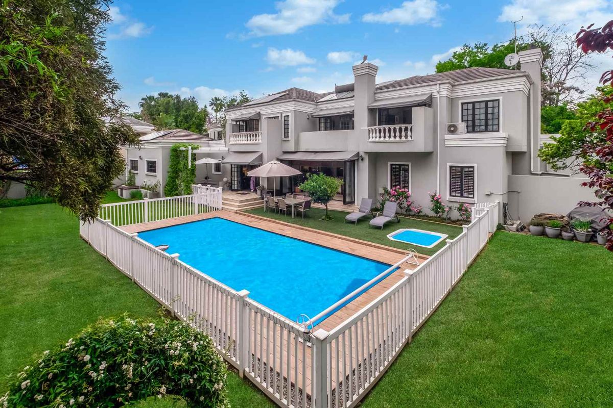 Spacious rear exterior view featuring a well-maintained swimming pool with safety fencing, a paved patio area, and a large two-story residence with balconies.