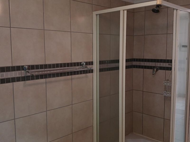 A functional bathroom featuring a corner shower enclosure with tiled walls and a built-in towel rail.