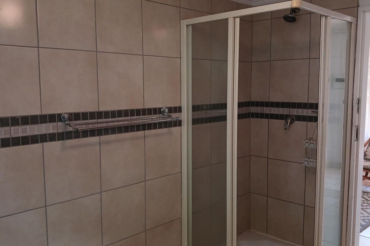 A functional bathroom featuring a corner shower enclosure with tiled walls and a built-in towel rail.