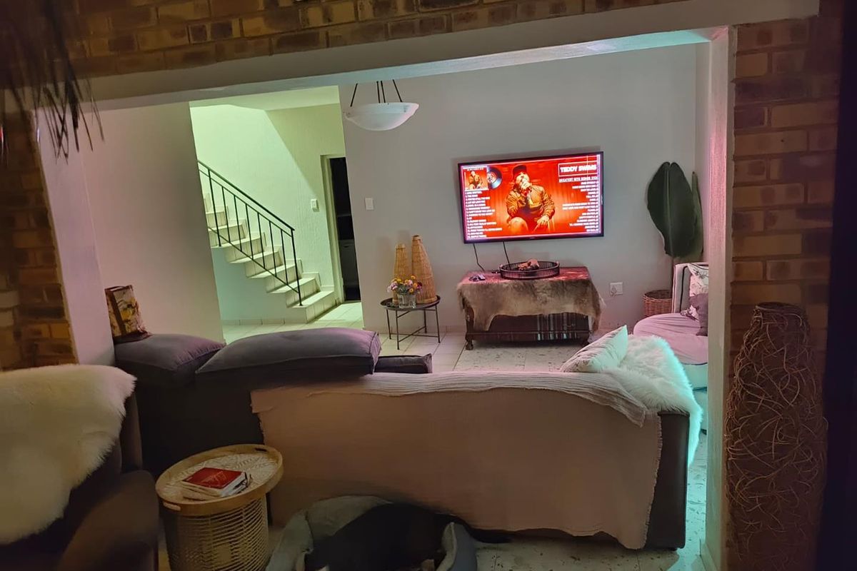 A living room area featuring exposed brick walls, tiled flooring, and an open-plan layout with a staircase leading to the upper level.