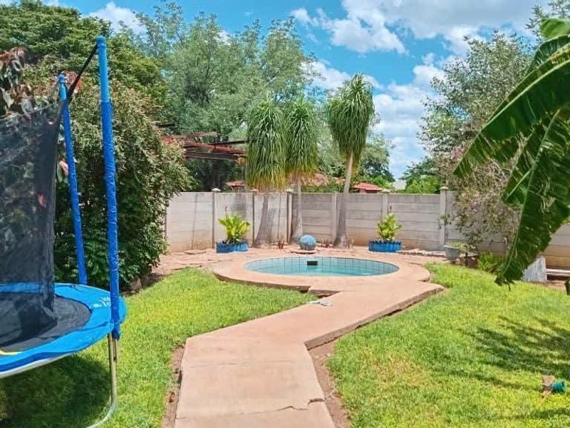 A backyard garden area featuring a small circular swimming pool, a paved walkway, and a concrete boundary wall.