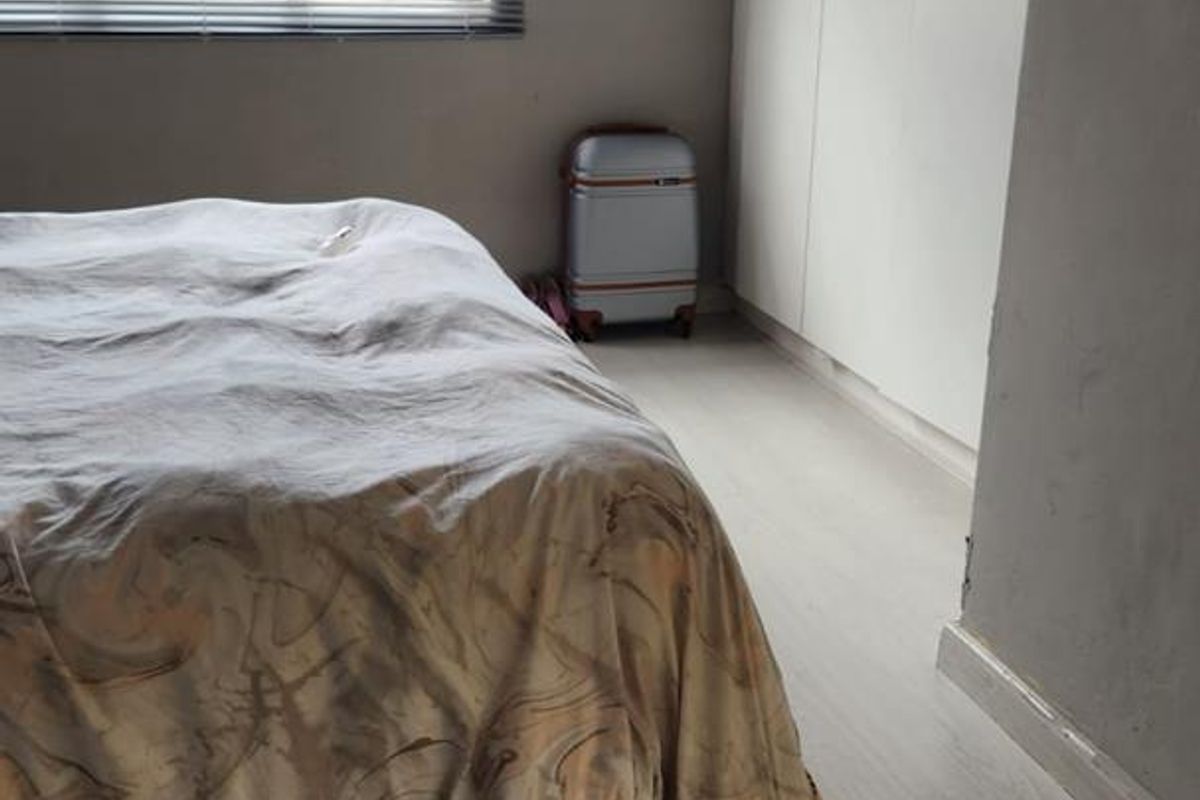 A bedroom featuring light-toned laminate flooring, built-in floor-to-ceiling wardrobes, and a window fitted with horizontal blinds.