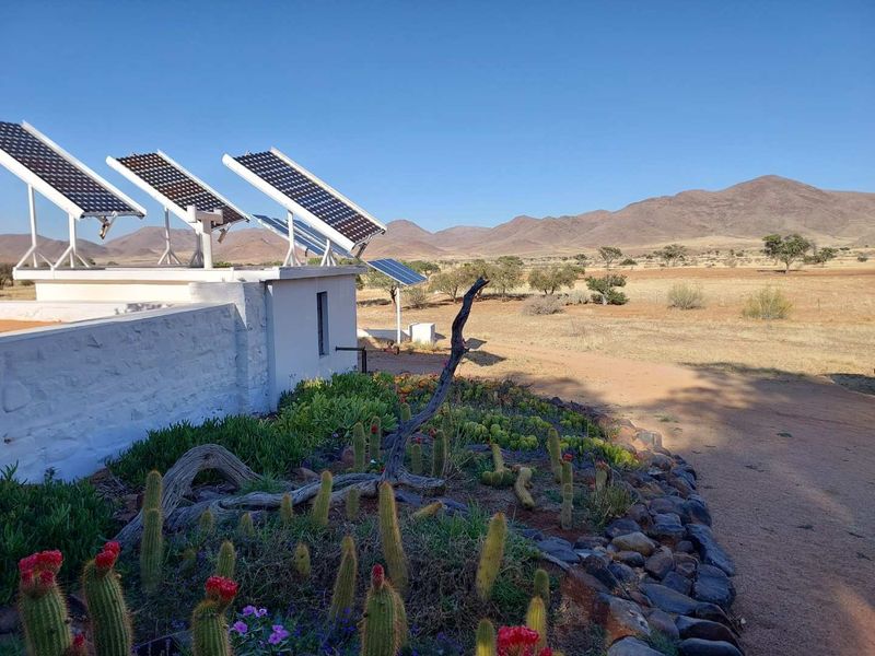 Exterior view of a farm property featuring a solar panel array mounted on a white stone structure, set against a scenic mountain landscape.
