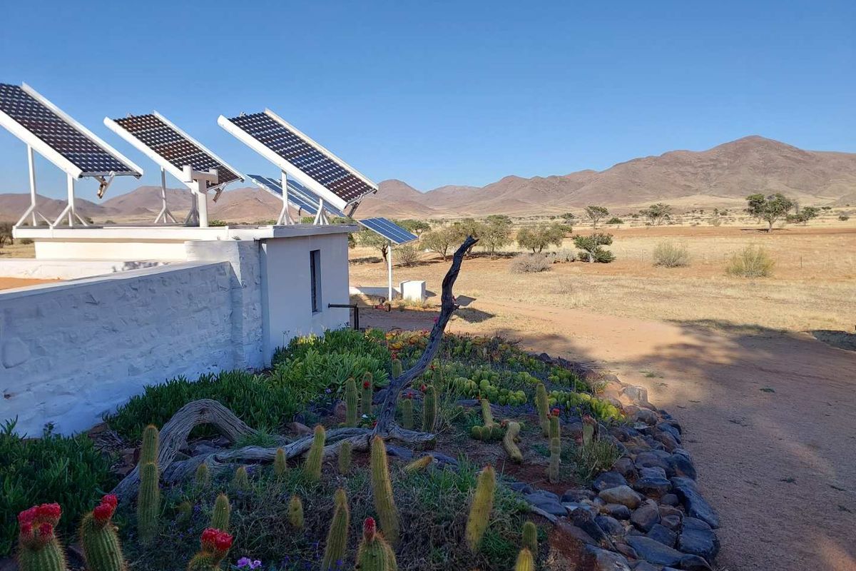 Exterior view of a farm property featuring a solar panel array mounted on a white stone structure, set against a scenic mountain landscape.