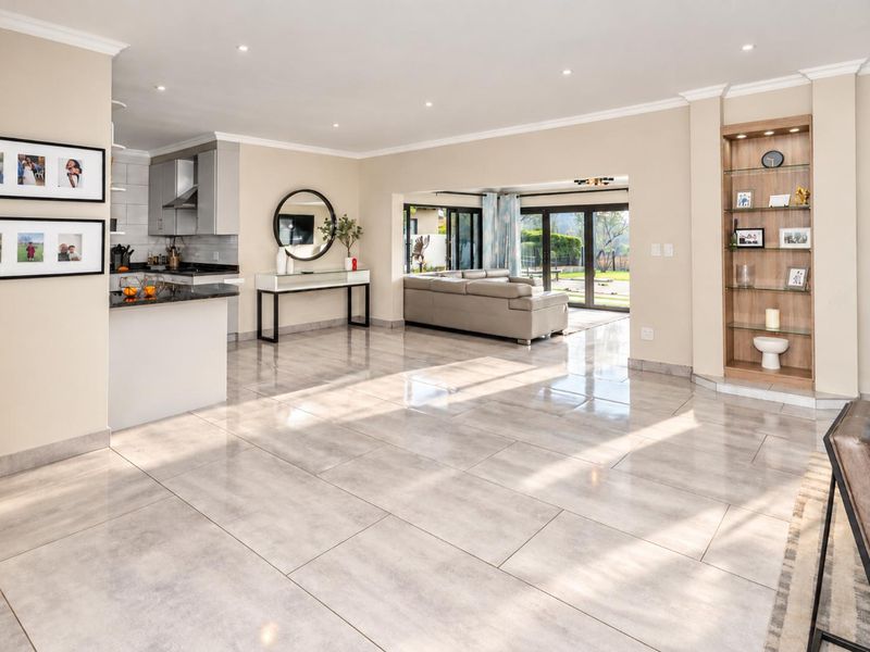 Spacious open-plan living area featuring polished tiled floors, recessed lighting, built-in display shelving, and a modern kitchen with granite countertops and seamless outdoor access.