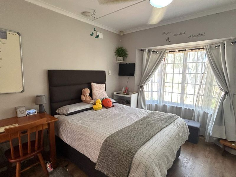 A cozy bedroom featuring laminate flooring, a large bay window allowing natural light, and a ceiling fan for climate control.