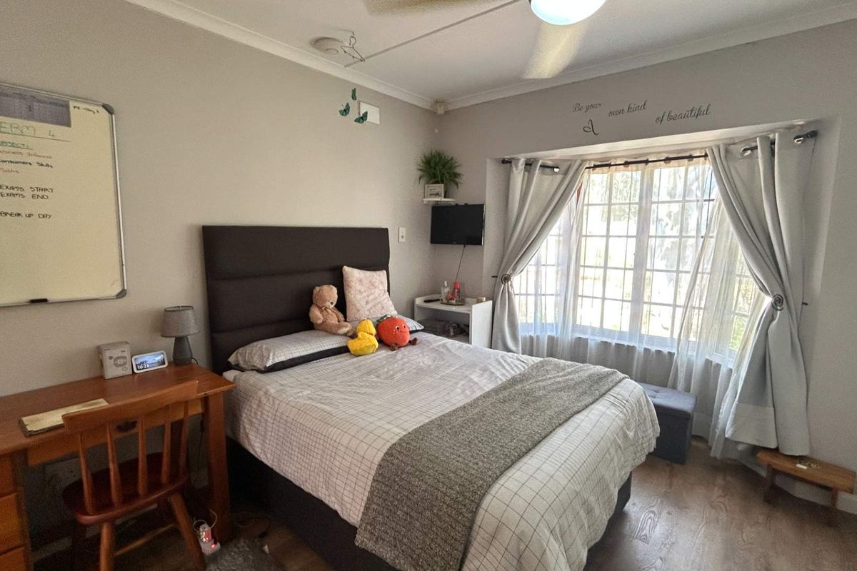 A cozy bedroom featuring laminate flooring, a large bay window allowing natural light, and a ceiling fan for climate control.