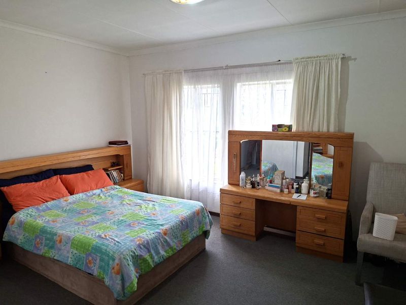 A spacious bedroom featuring carpeted flooring, large windows with security bars, and neutral wall finishes, offering a comfortable and functional living space.