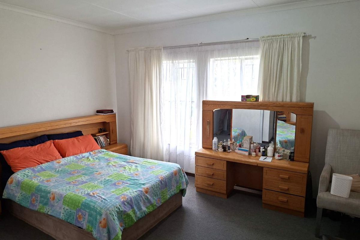 A spacious bedroom featuring carpeted flooring, large windows with security bars, and neutral wall finishes, offering a comfortable and functional living space.