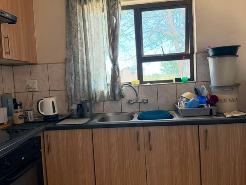 A functional kitchen featuring wood-look cabinetry, a double sink, built-in oven, and tiled splashback, requiring cosmetic updates to improve its overall aesthetic appeal.