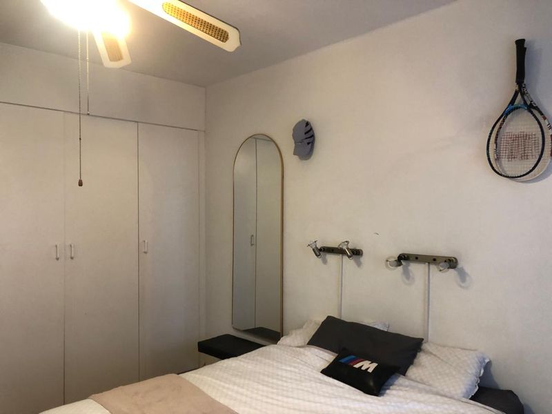 A functional bedroom featuring a built-in wardrobe, ceiling fan, and wall-mounted reading lights, offering a practical layout for comfortable living.