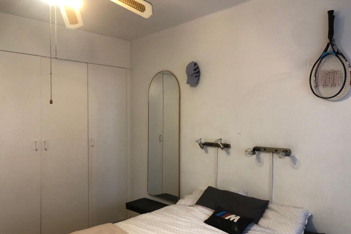 A functional bedroom featuring a built-in wardrobe, ceiling fan, and wall-mounted reading lights, offering a practical layout for comfortable living.
