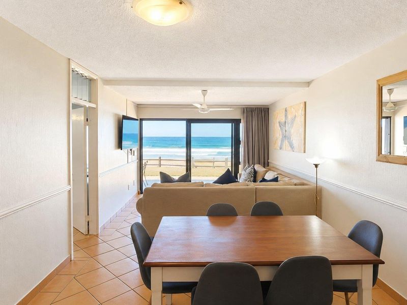 Open plan living and dining area featuring ceramic tile flooring, ceiling fan, and large sliding glass doors opening to a beach view.