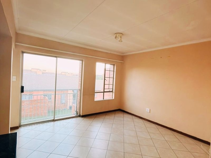 A bright, empty living area featuring neutral tiled flooring, large windows, and a sliding door providing access to the exterior.