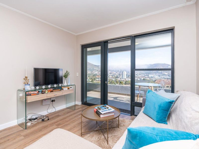 A bright living room featuring laminate flooring and large sliding glass doors that open onto a balcony with expansive city and mountain views.