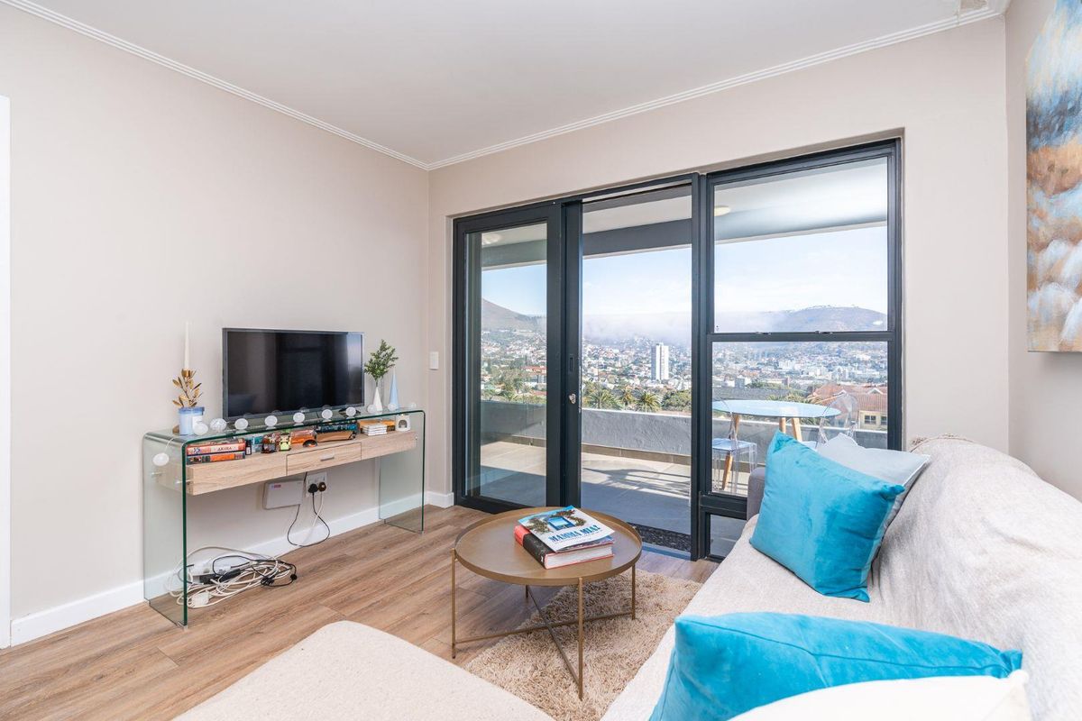 A bright living room featuring laminate flooring and large sliding glass doors that open onto a balcony with expansive city and mountain views.