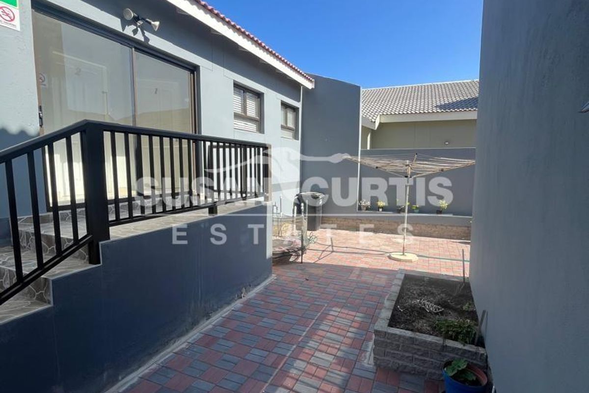A paved rear courtyard area featuring a raised patio section with black metal railings and a small built-in garden planter.