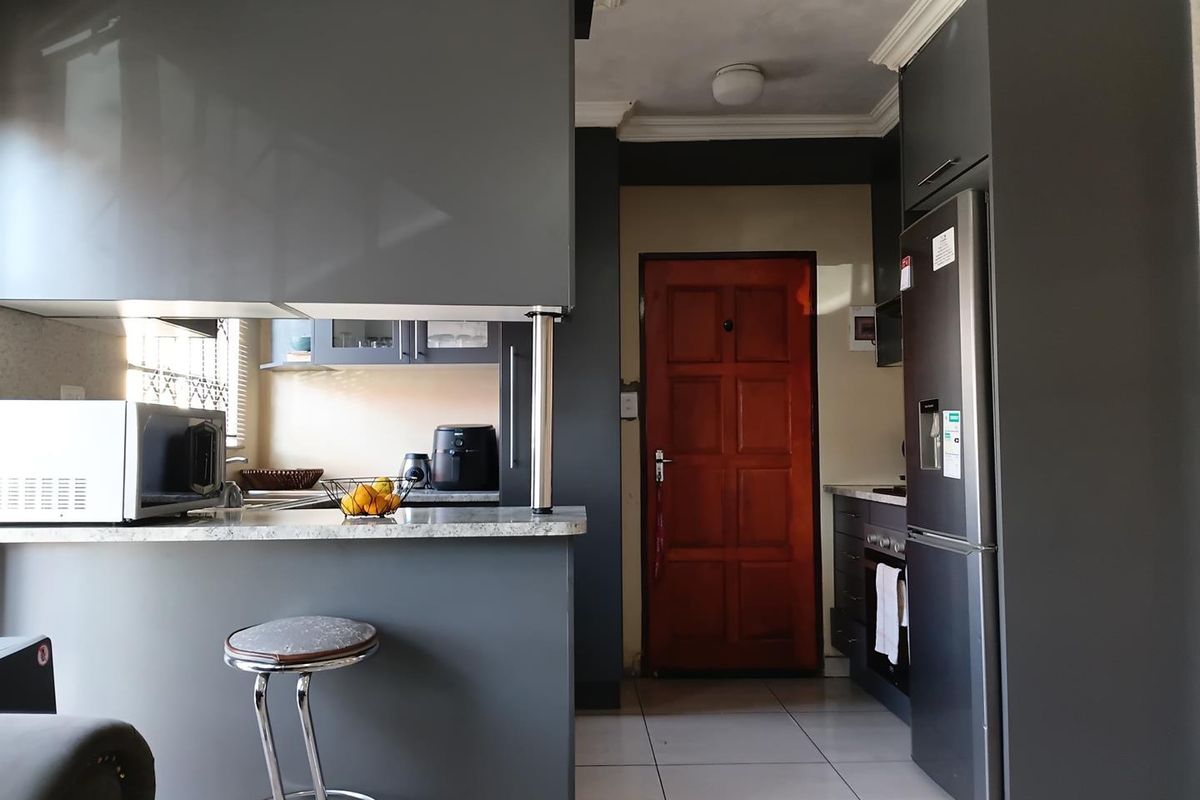 Modern kitchen featuring dark grey cabinetry, stone countertops, a breakfast bar, and tiled flooring, providing a functional and contemporary cooking space.