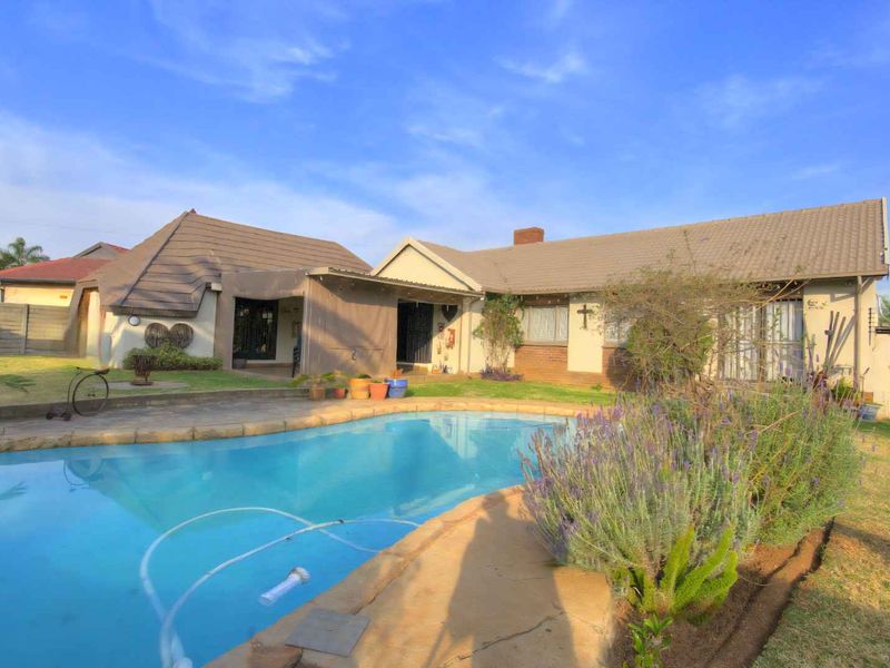 Rear exterior view of the house featuring a swimming pool, paved patio area, and established garden with brick and tiled roof construction.